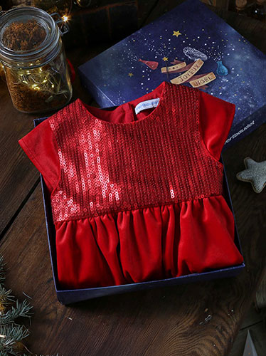 Robe de fête rouge à sequins pour enfant, présentée dans un coffret cadeau Vertbaudet avec un bandeau assorti, sur une table en bois décorée pour Noël.